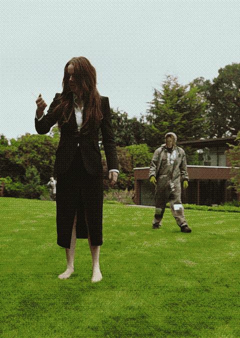 a screenshot of a film with a disheveled woman standing in a yard while a man in a beekeeping outfit stands at a distance behind her.