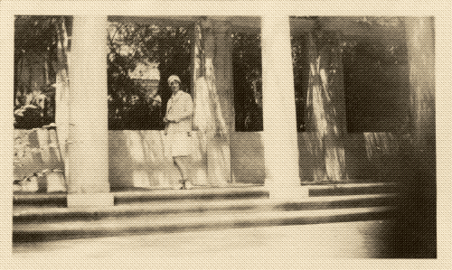 black and white photo of a woman standing at the top of a staircase between columns