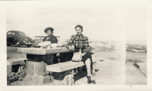 black and white photo of two women sitting at a picnic bench on the beach