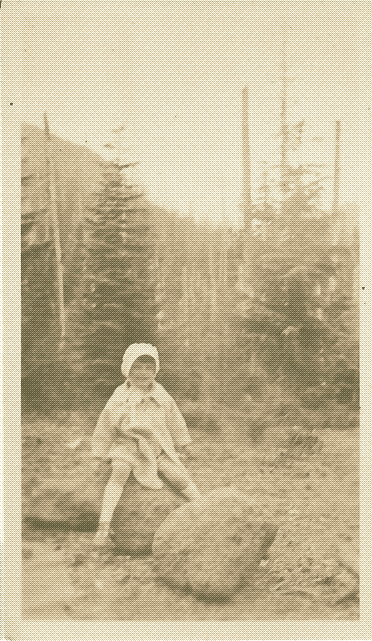 black and white photo of a group of a toddler-aged girl sitting on a rock with a forest and mountains in the background