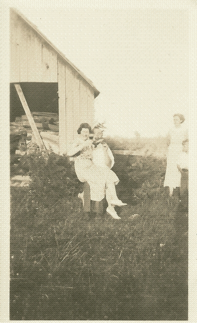 black and white photo of a woman with a glass of wine sitting on a man's lap in a chair in a yard