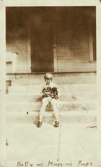 black and white photo of a young girl sitting on porch steps holding three puppies