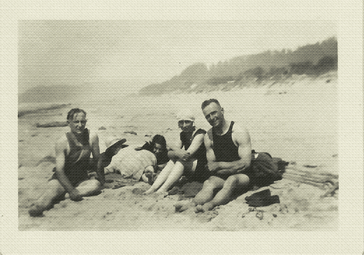 black and white photo of three women and two men sitting on a beach in their swimsuits