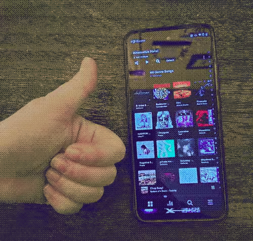 photograph of a smartphone displaying a music library with album art, with a hand giving a thumbs up next to it